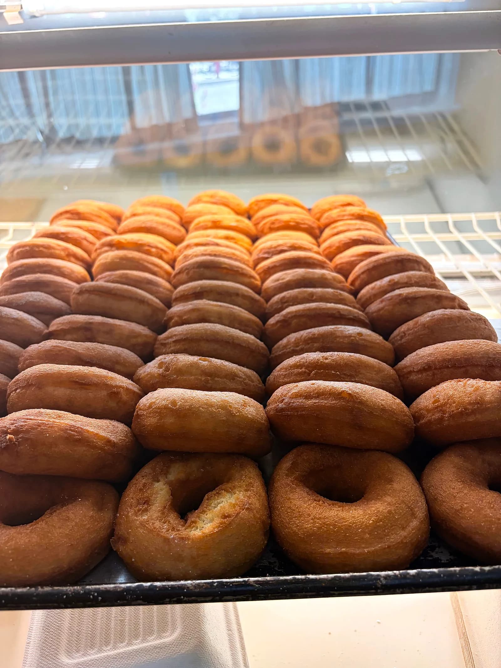 Trays of old-fashioned plain cake donuts stacked in the case
