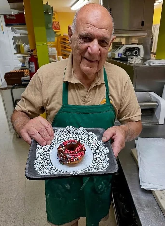 Tony, the owner of Marvel's Bakery, holding a fresh birthday donut in the kitchen